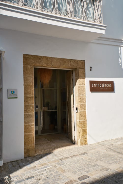 Entrada de EntreArcos Casa Eco-Boutique en Vejer de la Frontera con puerta de piedra y letrero