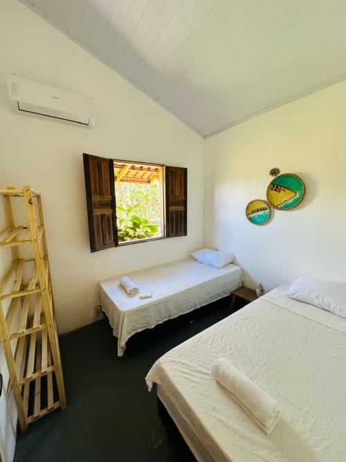 Quarto claro na Caraiva Cadu House com duas camas, janela de madeira, decoração litorânea e piso de azulejo escuro