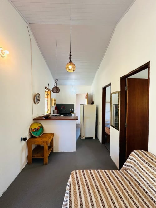 Interior aconchegante da Caraiva Cadu House com cama, cozinha compacta, luminárias pendentes e portas de madeira