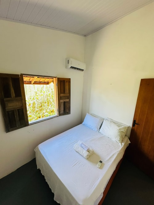 Quarto iluminado com cama queen, janela de madeira, ar condicionado e porta de madeira na propriedade beira-mar Caraiva Cadu House