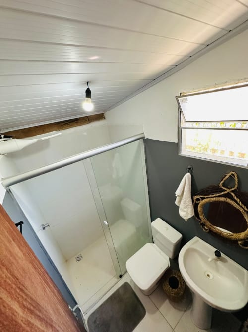 Banheiro moderno na Caraiva Cadu House com chuveiro, vaso sanitário, pia e decoração costeira com espelho de corda e toalheiro.