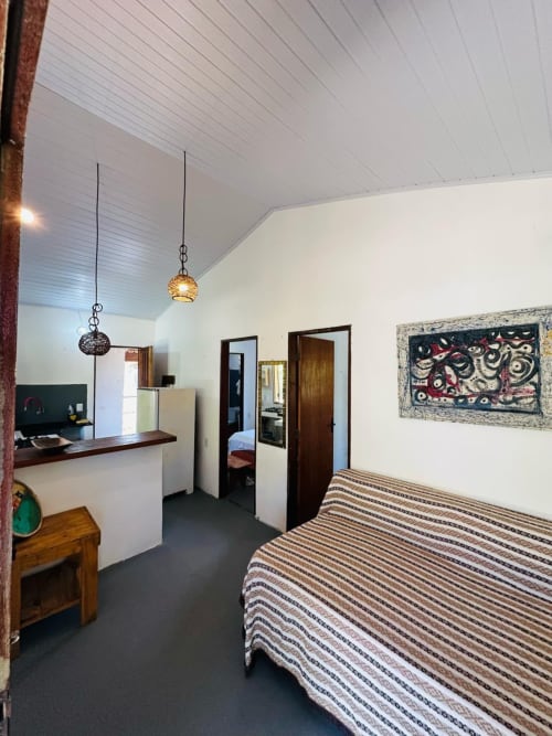 Quarto espaçoso com cama listrada, luminárias pendentes, kitchenette e obras de arte na Casa Caraiva Cadu