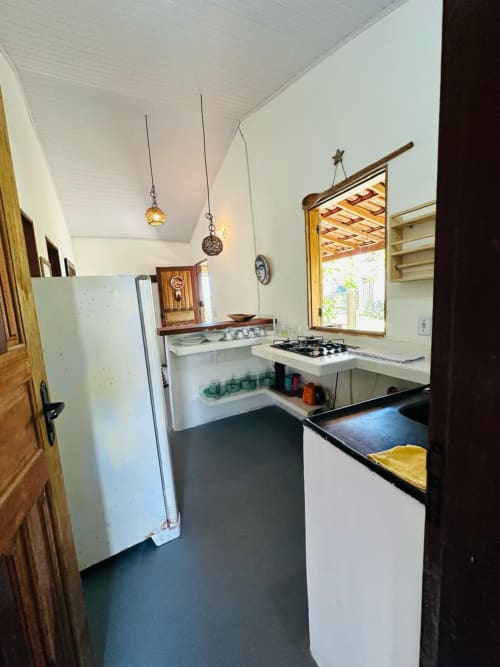 Cozinha compacta em apartamento à beira-mar de Caraiva com eletrodomésticos brancos, fogão a gás, luminárias pendentes e piso escuro