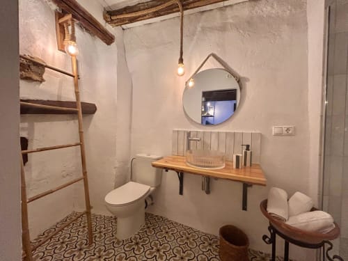 Baño rústico de Casa de la Aguadora con mueble de madera, espejo redondo, inodoro y piso con azulejos decorativos de patrón