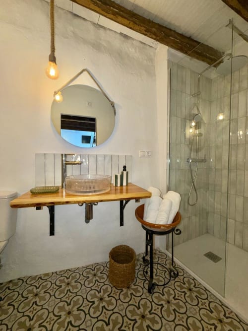 Baño moderno en Casa de la Aguadora con espejo redondo, tocador de madera, ducha tipo lluvia y azulejos con patrón en piso