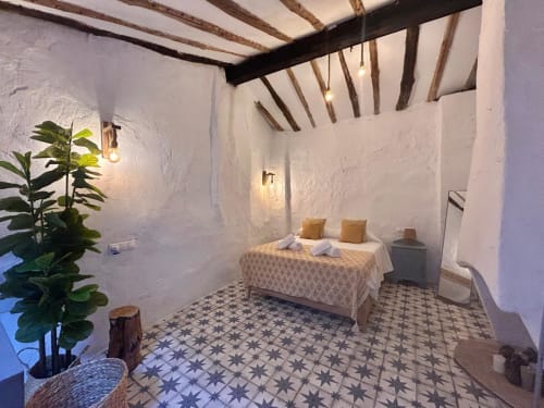 Dormitorio rústico en Casa de la Aguadora en Iznatoraf con vigas de madera vista, paredes blancas, suelo de azulejos decorados y cama con