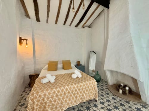 Acogedora habitación en Casa de la Aguadora en Iznatoraf con paredes blancas, vigas de madera, colcha beige y almohadas amarillas