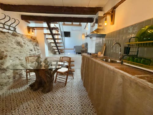 Cocina y comedor diáfanos con muros de piedra rústica, vigas de madera y suelo de azulejos estampados en Casa de la Aguadora