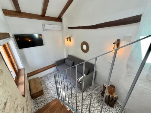 Zona de asientos de entresuelo en la sala Real de Casa de la Aguadora con vigas de madera vista, barandilla gris y televisor de pantalla plana