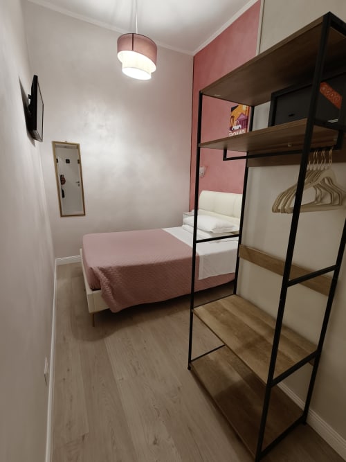 Camera singola economy dell'Hotel Principe Amedeo con parete accent rosa, letto a soppalco, scaffalatura e illuminazione a sospensione
