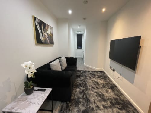 Modern one-bedroom suite at Empire Serviced Apartments in Leicester with black sofa, wall-mounted flat screen TV, and marble