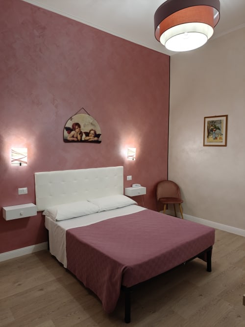 Camera matrimoniale Economy dell'Hotel Principe Amedeo con parete accento malva, testata bianca e moderna lampada a soffitto