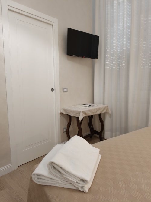 Camera Triple Economy dell'Hotel Principe Amedeo con TV a parete, tavolo in legno con tovaglia beige e biancheria bianca sul pavimento