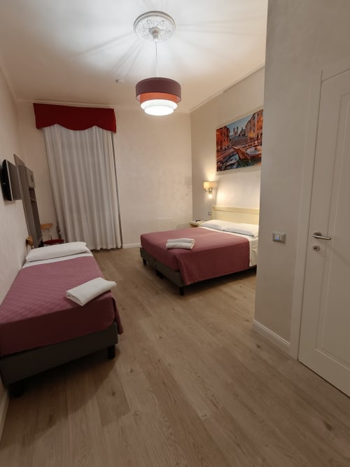 Camera tripla economy dell'Hotel Principe Amedeo con due letti, biancheria bordeaux, pavimento in legno e vista sulla città in Italia