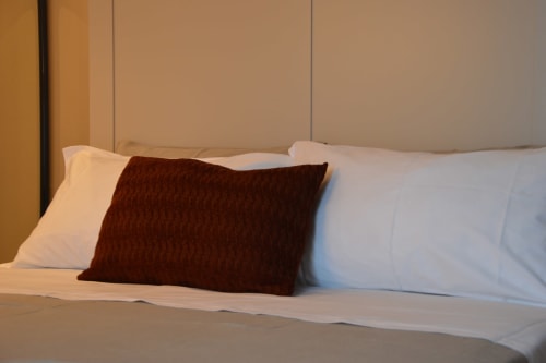 Lussuoso letto di Villa Rosati con cuscini bianchi, cuscino accentato bordeaux e testiera beige nella camera Resina