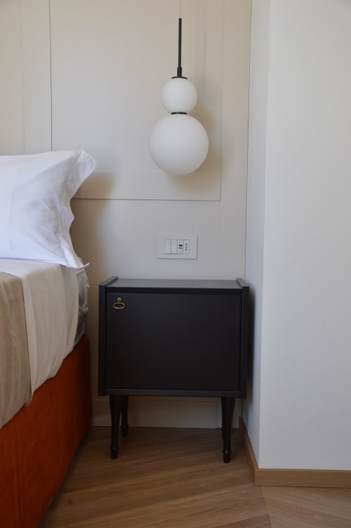 Angolo camera minimalista di Villa Rosati con lampada a sospensione bianca, comodino nero e biancheria bianca a Sanzeno