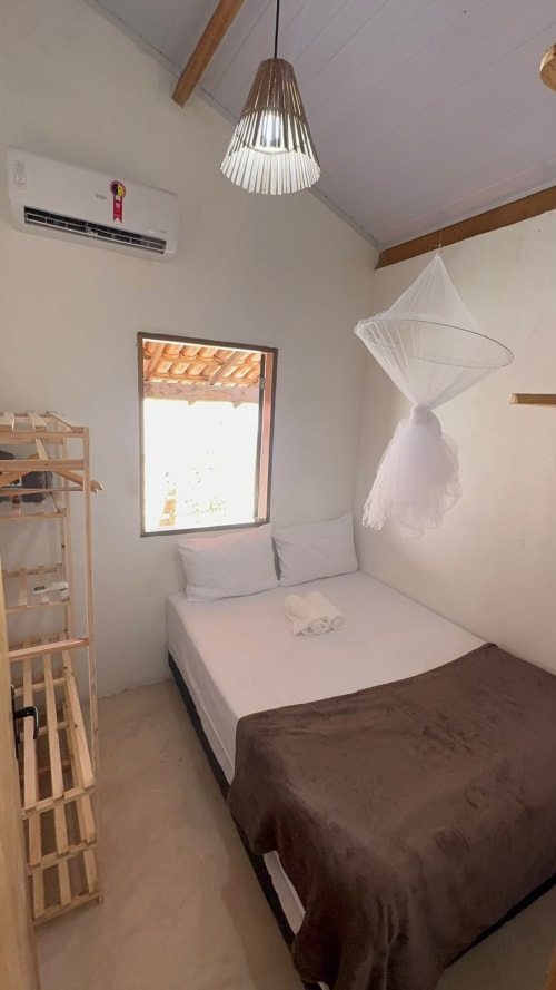 Quarto luminoso na Caraiva Cadu House com cama, mosquiteiro, luminária pendente e janela com vista para o exterior