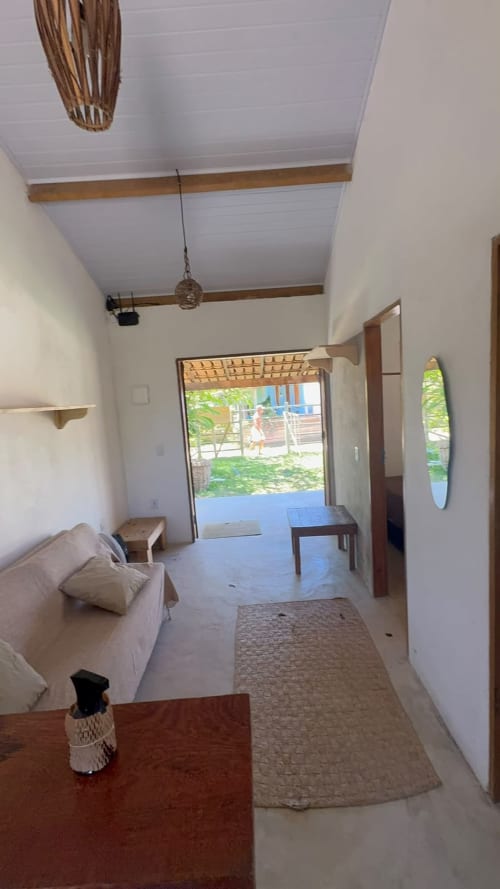 Luminosa sala de estar da Caraiva Meynha House com teto de vigas, sofá e portas abertas para jardim privado e área de pátio