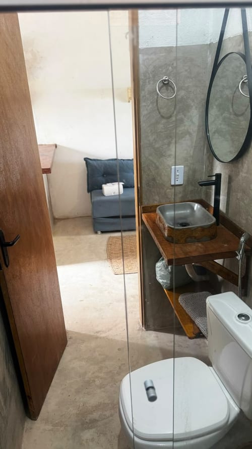 Banheiro moderno na Caraiva Cadu House com cuba vessel, sanitário, espelhos e box em vidro aberto para o quarto.