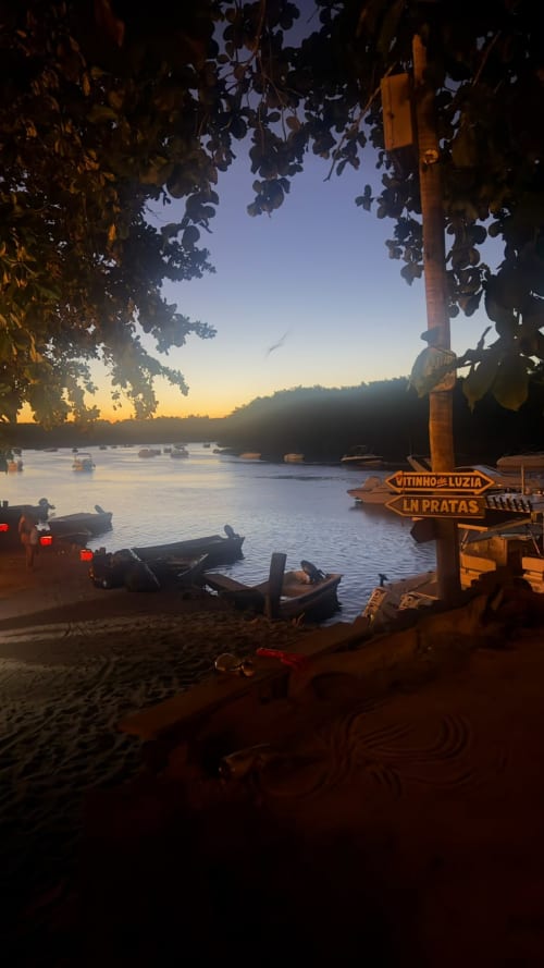 Pôr do sol na praia de Caraiva com barcos de pesca tradicionais e placa de madeira, hospedagem em Porto Seguro com vista para a orla.