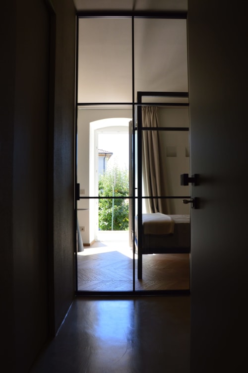 Porte in vetro con cornice nera che si aprono sulla vista del giardino di Villa Rosati a Sanzeno, con camera da letto e luce naturale visibile