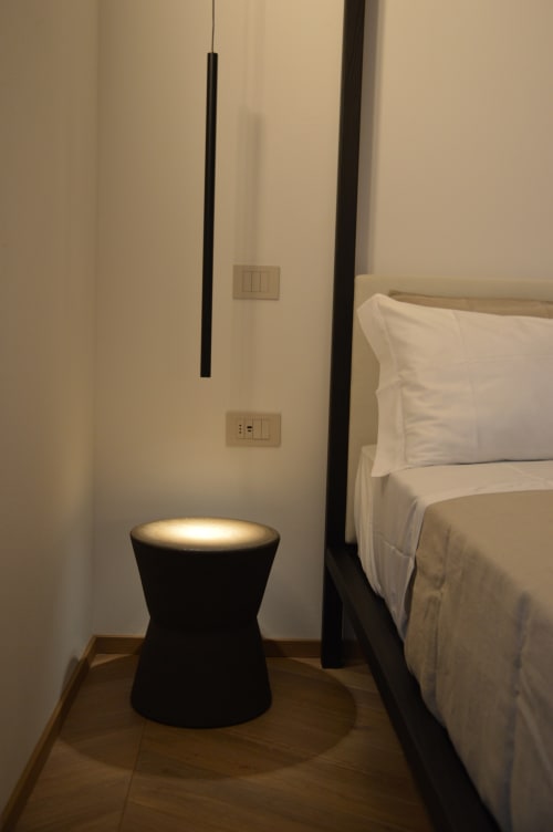 Lampada a sospensione nera moderna e tavolino cilindrico nella camera da letto di Villa Rosati con biancheria bianca e pavimentazione in legno