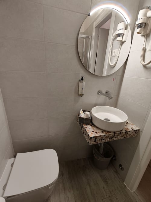 Bagno moderno dell'Hotel Principe Amedeo con specchio rotondo illuminato, lavabo bianco a semincasso, water e finiture in legno scuro