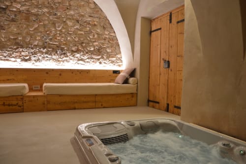 Camera spa di Villa Rosati con vasca idromassaggio, letto in legno e muro in pietra a Sanzeno