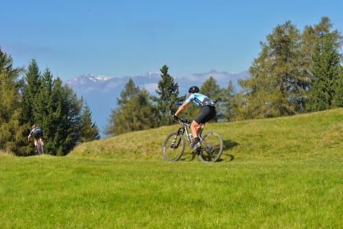 Ciclista in sella sulla prateria alpina presso Villa Rosati a Sanzeno, Trentino, con le vette alpine sullo sfondo