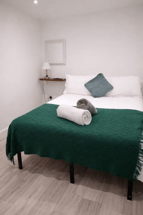 Modern bedroom at La Rose Serenity Residence with green quilted throw, white pillows, and bedside lamp in London