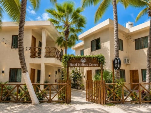 Entrada frente al mar del Hotel Holbox Centro con palmeras, arquitectura colonial color crema, barandales de madera y ambiente tropical