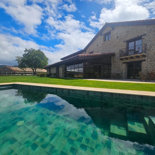 Hotel Izarbe en Burgos: edificio de piedra con piscina, jardín cuidado y vistas a las montañas bajo cielo azul