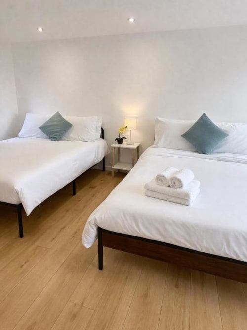 Twin bedroom at Victoria House Cozy Rooms London with white bedding, green cushions, and wooden floor.