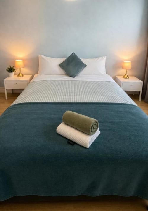 Cozy bedroom at Victoria House London with queen bed, teal bedding, white pillows, brass lamps, and rolled towels