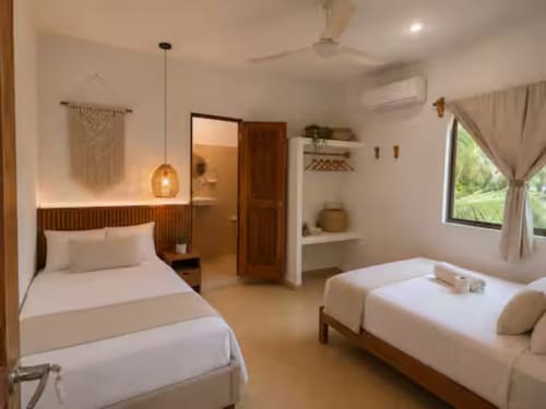 Suite moderna del Hotel Holbox Centro con dos camas, detalles de madera, iluminación colgante, baño privado y vistas al jardín