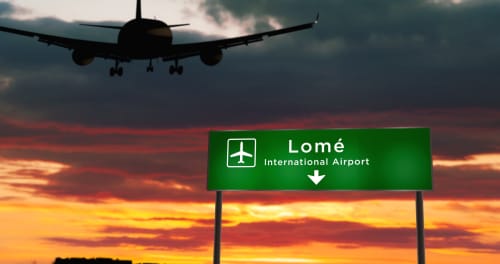 Avion s'approchant de l'aéroport international de Lomé au coucher du soleil, enseigne de l'auberge Nomads Kodjoviakopé visible au Togo