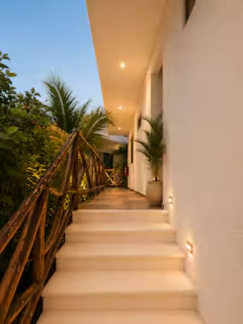Pasillo moderno iluminado del Hotel Holbox Centro con paredes blancas, plantas tropicales y barandales de madera al atardecer
