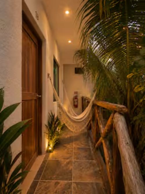 Elegante pasillo del Hotel Holbox Centro con plantas tropicales, puertas de madera, hamaca e iluminación cálida