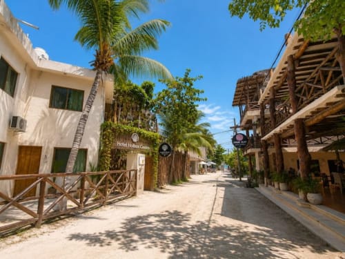 Vista de la calle del Hotel Holbox Centro con edificio colonial blanco, palmeras y estructuras de madera rústica en Holbox, México