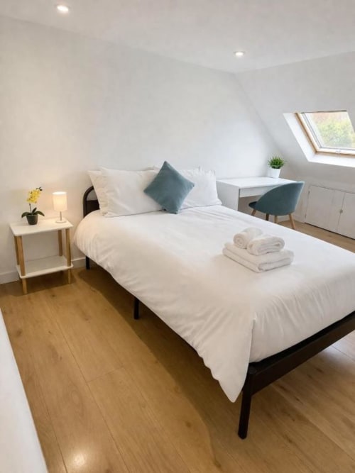 Modern attic bedroom at Victoria House Cozy Rooms, London with white bedding, skylight, desk, and wooden flooring