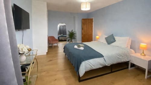 Modern bedroom at Victoria House Cozy Rooms in London with queen bed, TV, seating area, and wooden flooring