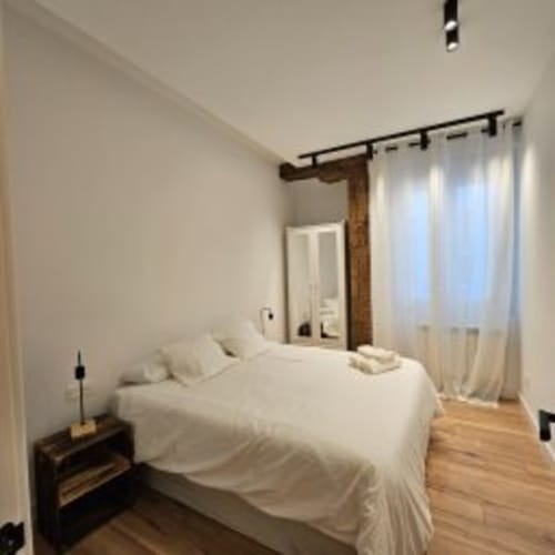 Luminosa habitación en el Hotel Izarbe de Burgos con ropa de cama blanca, suelo de madera y cortinas translúcidas