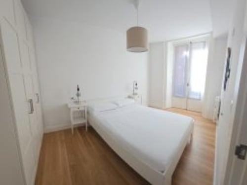 Habitación moderna del Hotel Izarbe en Burgos con cama blanca, suelos de madera, lámpara colgante y puertas de cristal