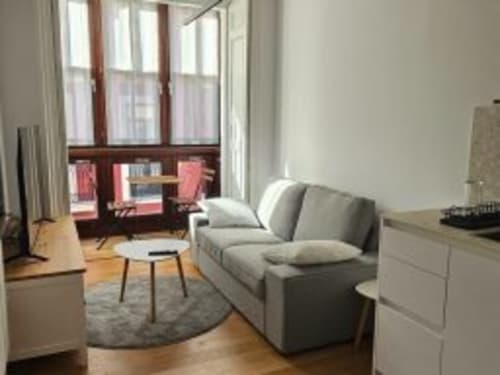 Habitación moderna del Hotel Izarbe en Burgos con sofá gris, decoración minimalista, suelos de madera y vistas al balcón
