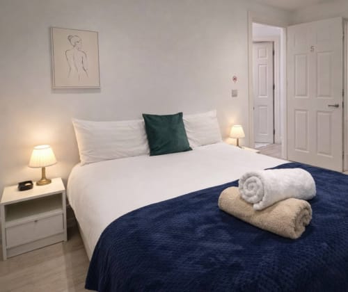 Modern bedroom at Victoria House Cozy Rooms, London B&B with white bedding, dark blue throw, green cushion, rolled towels,