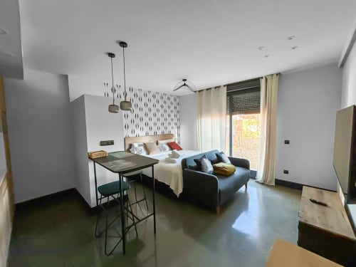 Estudio moderno en Madrid Río con cama, sofá, mesa comedor, luces colgantes y vistas de la ciudad a través de amplios ventanales