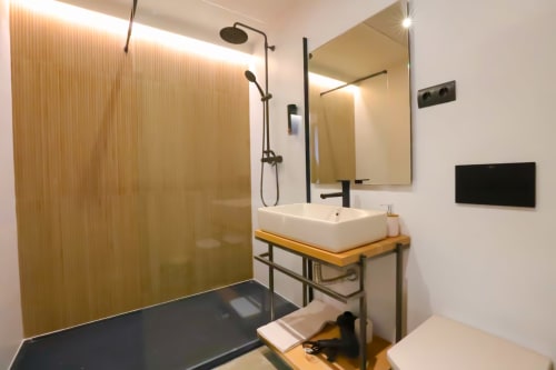 Baño moderno en apartamento madrileño con ducha a ras de suelo, lavabo de cerámica, espejo calefactable y detalles en madera