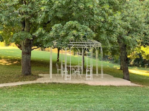 Schattiger Pergola-Sitzbereich umgeben von alten Bäumen auf gepflegtem Rasen in der Domaine de Bize, Mirepoix
