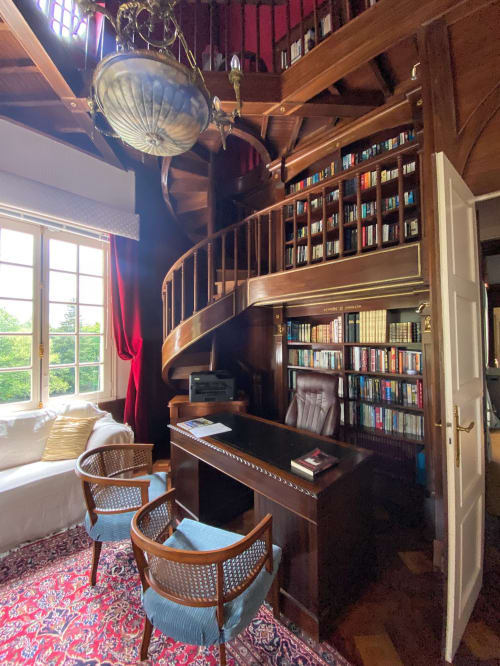 Elegante Studiobibliothek mit Wendeltreppe, hölzernen Bücherregalen, Schreibtisch und Spitzbogenfenstern mit Bergblick