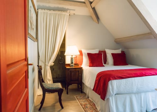 Elegantes Dachzimmer mit roten Akzenten, weißer Bettwäsche, Holzbalken und Bergblick im Domaine de Bize Mirepoix